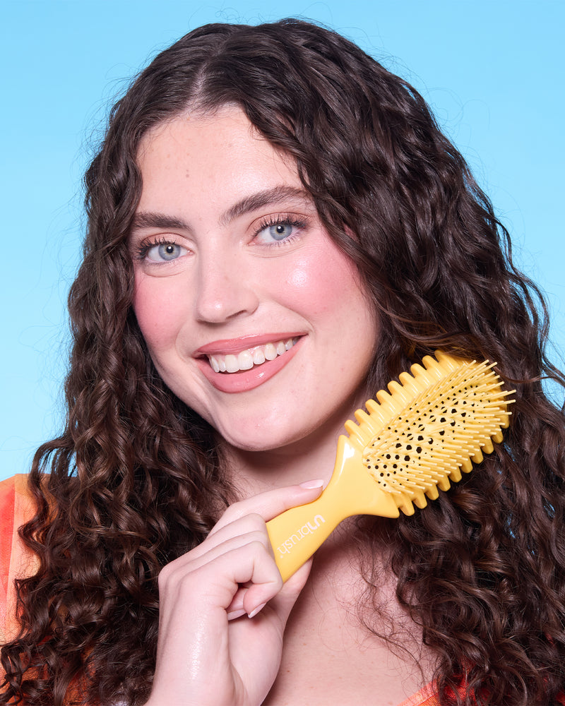 Woman with curly hair holding a yellow hairbrush against a blue background