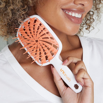 Model holding the UNbrush Plus Orange Sherbet Detanging Hair Brush