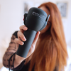 Model posing in front of camera while holding the hair dryer in front of camera and her face.