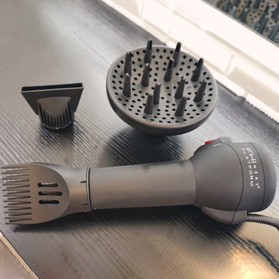 Hair dryer with the straightening comb attached is laid flat on a surface next to two other hair dryer attachments.